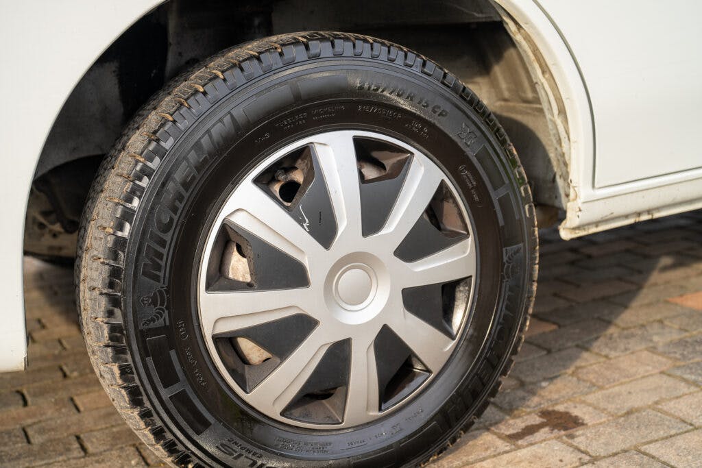 This image shows a close-up of a Michelin tire mounted on a silver alloy wheel with a multi-spoke design, characteristic of the 2006 Auto-Sleepers Nuevo EK. The tread pattern and wheel are clean, and the car's body is partially visible above the tire.