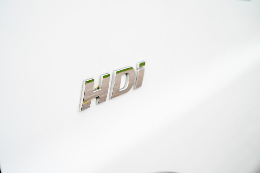Close-up view of a metallic "HDI" badge on the white body of a 2006 Auto-Sleepers Nuevo EK. The letters are slightly raised and reflective.