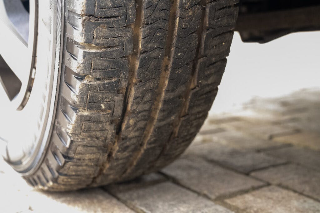 A close-up image of a car tire showing the tread pattern from a side view. The tire, possibly belonging to a 2006 Auto-Sleepers Nuevo EK, has visible signs of wear and is parked on a paved surface made of interlocking bricks.