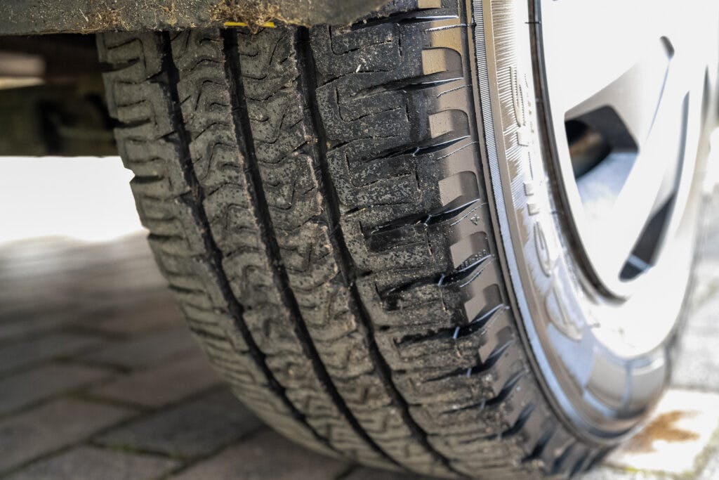 Close-up view of a car tire with visible tread patterns and slight dirt accumulation on the tire, possibly from extended travels in a reliable 2006 Auto-Sleepers Nuevo EK. The background shows a paved surface.