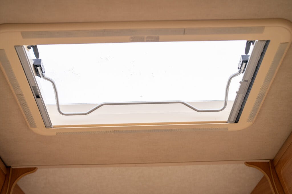 Image of an open rectangular skylight viewed from the interior of a 2006 Auto-Sleepers Nuevo EK. The skylight frame is beige, and the bright daylight is visible through the opening. The surrounding ceiling is also beige.