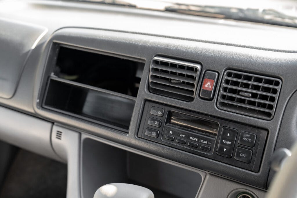 The image shows a close-up of a 2006 Mazda Bongo Friendee's dashboard. It features air conditioning vents, control buttons for temperature and airflow, and an empty slot where a stereo or other device might typically be installed. The dashboard appears to be in a light-colored interior.