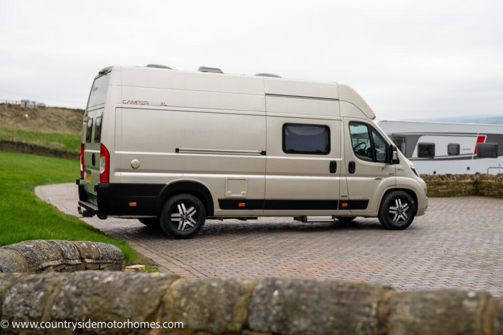 A beige 2020 Rapido Dreamer Select Campervan XL is parked on a cobblestone driveway with countryside views. The campervan has tinted windows and is labeled "Camper X3." The background includes a stone wall and another motorhome. The image features the text "www.countrysidemotorhomes.com.