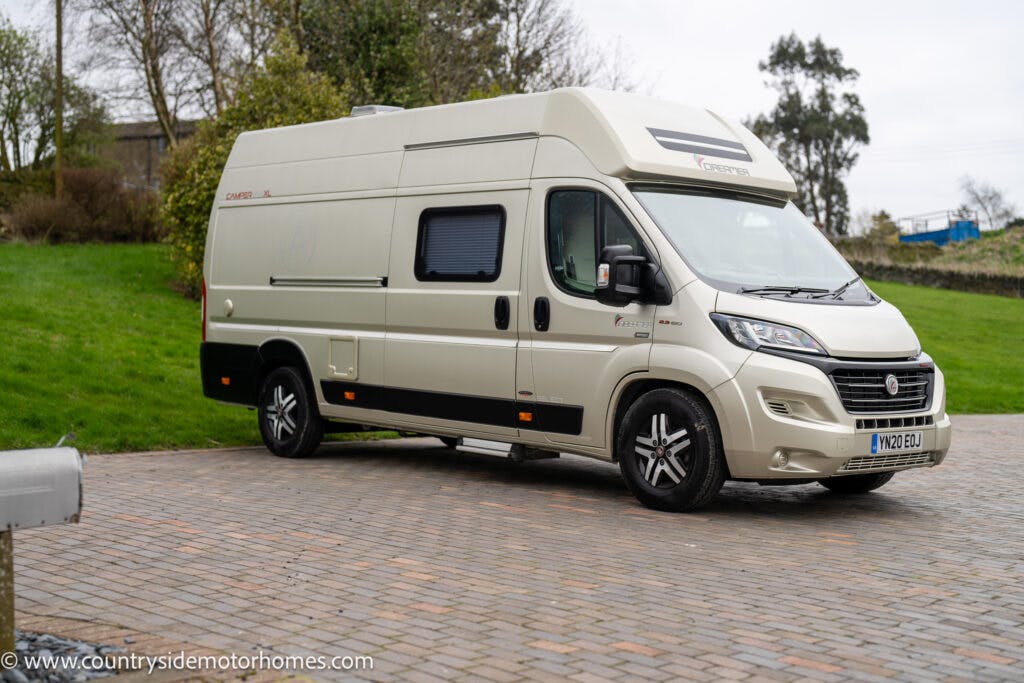A beige 2020 Rapido Dreamer Select Campervan XL is parked on a paved driveway with a grassy area and some trees in the background. The campervan has a high roof and tinted windows. A web address "www.countrysidemotorhomes.com" is visible at the bottom left corner of the image.