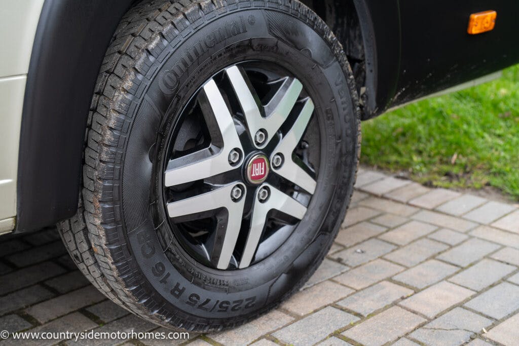 Close-up of a vehicle tire mounted on an alloy wheel. The tire, branded "Continental" with dimensions "225/75 R16 C," is part of the 2020 Rapido Dreamer Select Campervan XL. The wheel cap displays the Fiat logo. The vehicle is parked on a paved surface next to a grassy area.