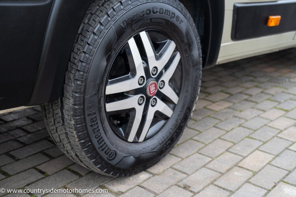 Close-up of a Continental VancoCamper tire on a 2020 Rapido Dreamer Select Campervan XL parked on a cobblestone surface. The tire is mounted on a black and silver alloy wheel. The image also partially shows the vehicle's beige body. The website "www.countryside-motorhomes.com" is visible.