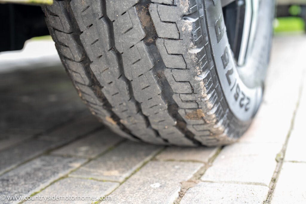 Close-up view of a 2020 Rapido Dreamer Select Campervan XL's tire on a paved surface. The tire tread pattern is clearly visible, with some dirt on parts of the tire. A small section of the vehicle's undercarriage is also visible. The image includes a watermark from countrysidemotorhomes.com.