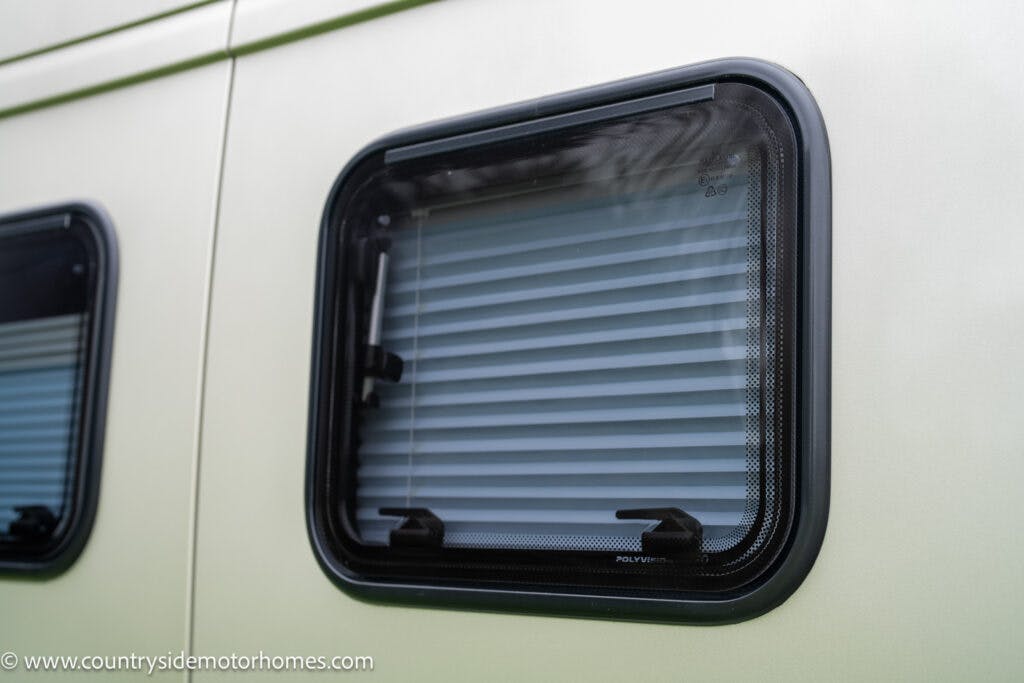 Close-up of a rectangular window on a 2020 Rapido Dreamer Select Campervan XL, partially covered with a white shade. The window has a black frame and is set against a light-colored exterior. The website www.countrysidemotorhomes.com is visible in the corner of the image.