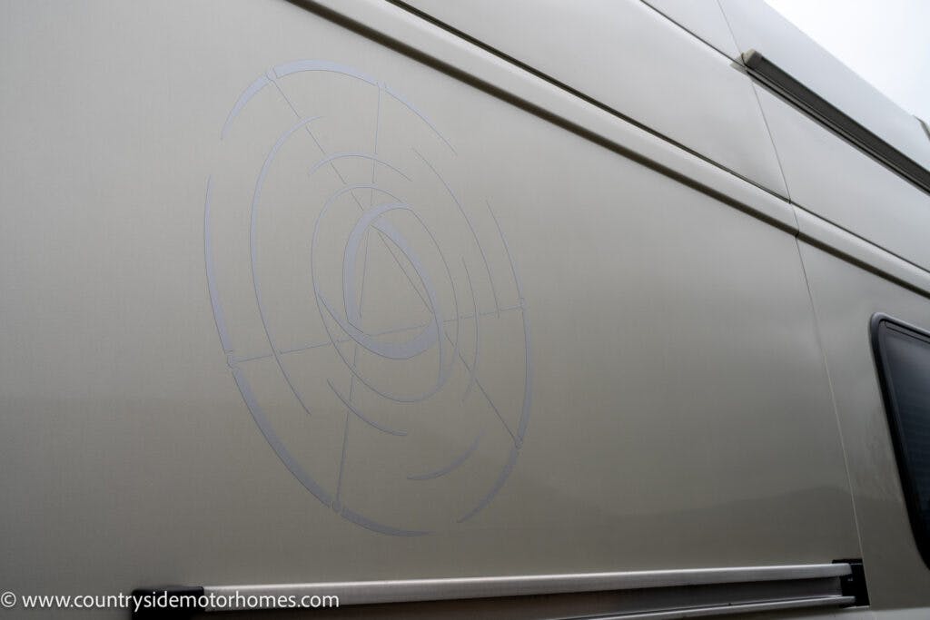 The photo shows the side of a beige 2020 Rapido Dreamer Select Campervan XL with a circular graphic design. The design includes multiple intersecting lines creating a target-like pattern. The website www.countrysidemotorhomes.com is visible in the bottom left corner.
