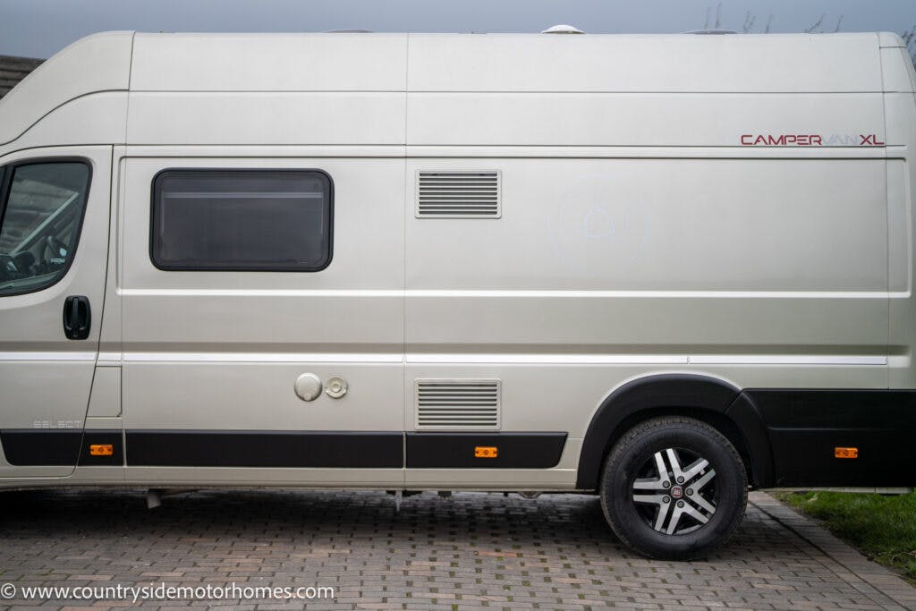 A side view of a 2020 Rapido Dreamer Select Campervan XL parked on a paved area. The vehicle has a black band along the bottom, several ventilation grilles, and a large tinted window. The website "www.countrysidemotorhomes.com" is visible on the bottom left corner of the image.