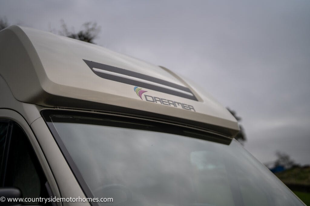 Close-up of the upper portion of a 2020 Rapido Dreamer Select Campervan XL with the logo "Dreamer" visible on the front. The background shows an overcast sky and blurred greenery. The website "www.countrysidemotorhomes.com" is visible in the bottom left corner.