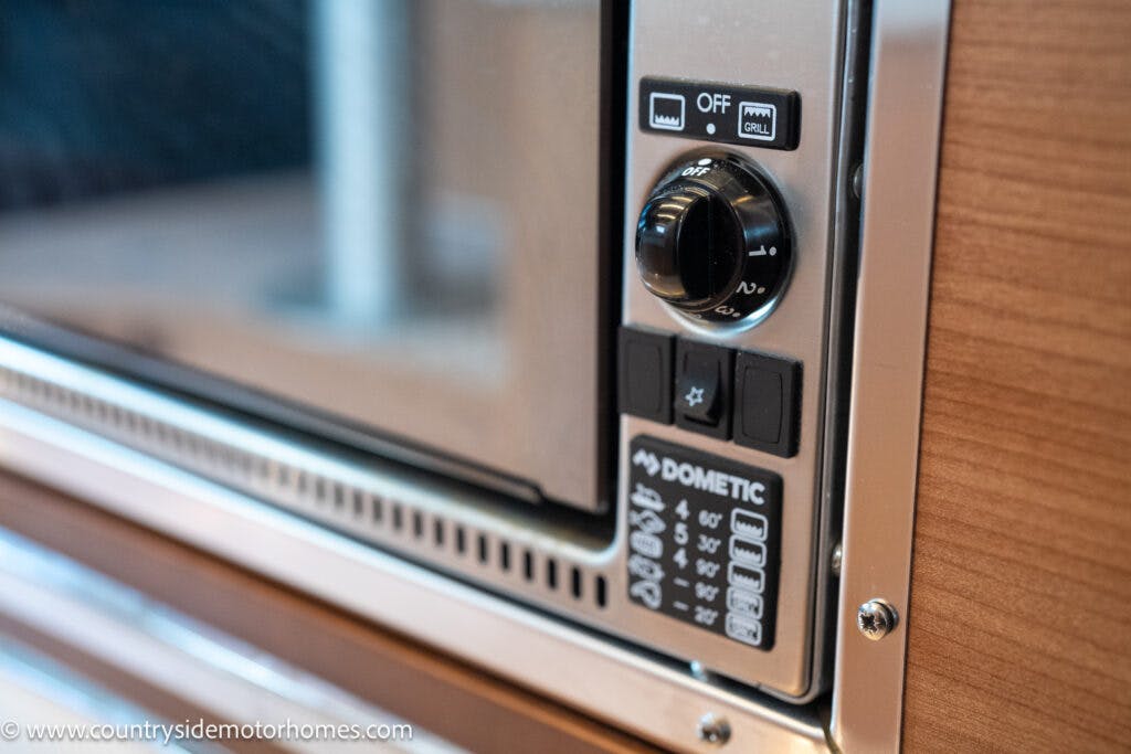 Close-up of a Dometic microwave control panel in the 2020 Rapido Dreamer Select Campervan XL, showing a dial for power levels marked OFF, GRILL, 1 to 4, and several buttons with various icons. The background includes part of a wooden cabinet. The website "countrysidemotorhomes.com" is visible.
