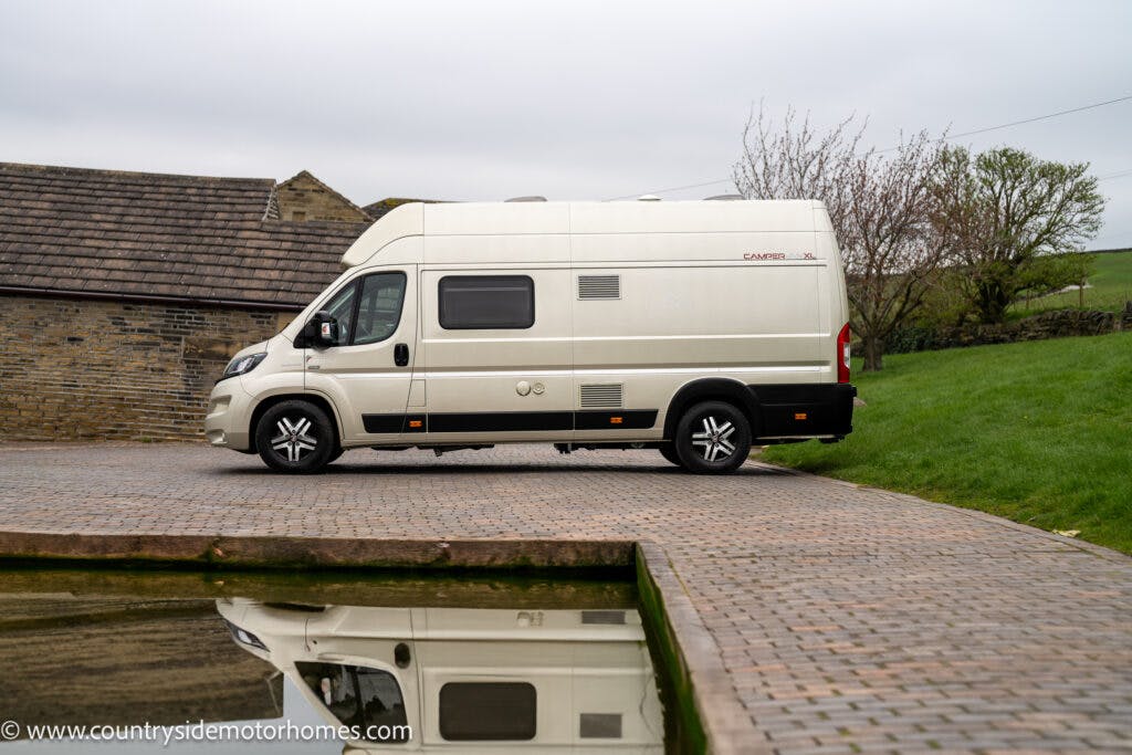 A white 2020 Rapido Dreamer Select Campervan XL is parked on a paved area beside a pond. Behind the van are two buildings and a grassy hill. The sky is overcast. A web address, www.countrysidemotorhomes.com, is visible in the bottom left corner of the image.