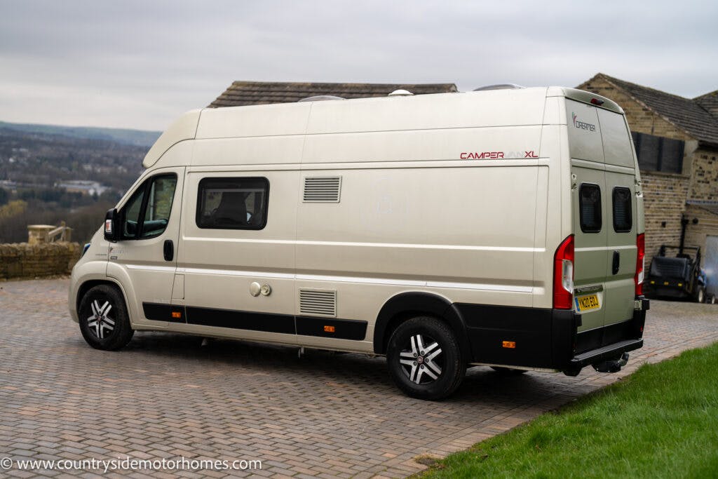 A white 2020 Rapido Dreamer Select Campervan XL, marked "Camper XL," is parked on a paved driveway with green grass on the side. Visible behind the camper is a stone structure and a hilly landscape in the background. The image is credited to "countrysidemotorhomes.com" at the bottom left.