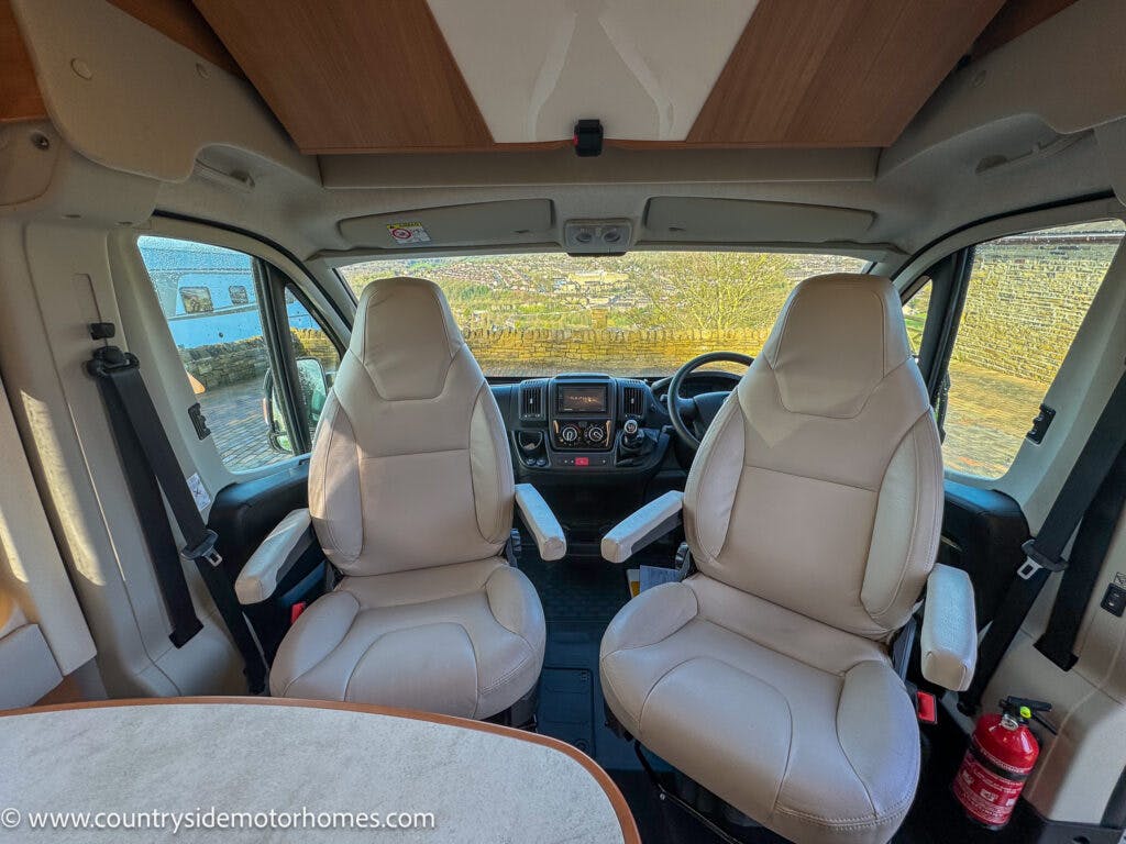 Interior view of a 2020 Rapido Dreamer Select Campervan XL showing the driver's and passenger's seats in the front cabin. A steering wheel, dashboard, and control panel are visible. A fire extinguisher is mounted to the side. The website www.countrysidemotorhomes.com is visible on the seat.