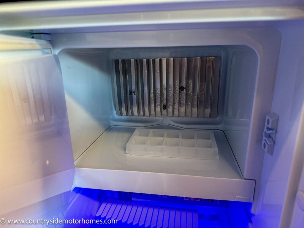 A close-up view of an open empty freezer compartment with an ice tray inside, showing the metal cooling element in the back. The image, tagged with "www.countrysidemotorhomes.com," highlights a feature of the 2020 Rapido Dreamer Select Campervan XL.