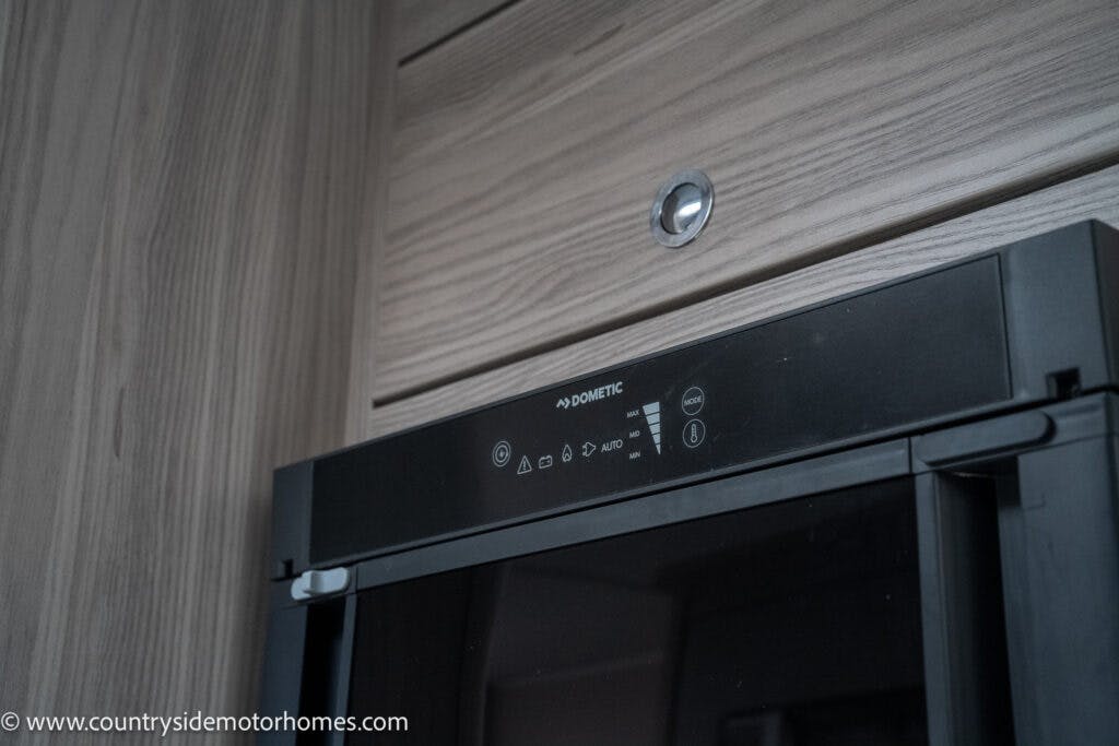 A close-up view of a Dometic microwave installed in the elegant wooden cabinetry of the 2022 Elddis Autoquest Lombardi 150 Masters Collection. The microwave features a digital control panel with various settings, seamlessly blending with the light wood grain finish. A watermark from www.countrysidemotorhomes.com is visible in the lower-left corner.