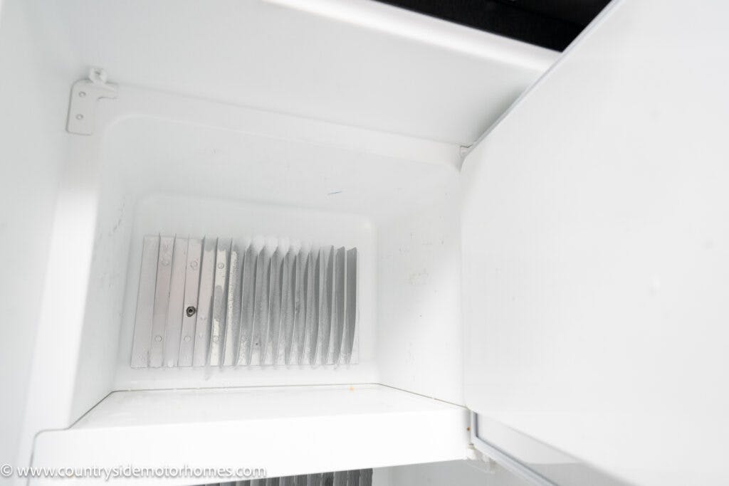 This image shows the interior of an empty freezer. The freezer has a white interior with a metallic vent at the back. The door is partially open, revealing the empty compartment. The words "countryside motorhomes" and "2022 Elddis Autoquest Lombardi 150 Masters Collection" are visible in the bottom left corner.