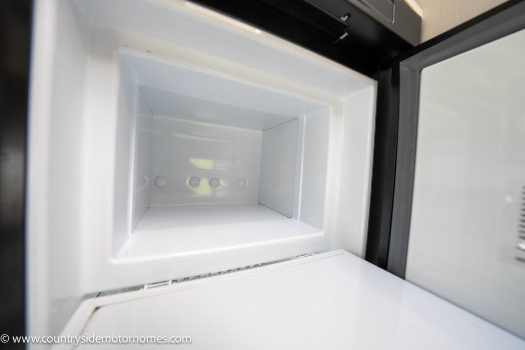 An empty white freezer compartment inside an open refrigerator in the 2021 Chausson 778 Premium. The interior surface is clean and shiny, with a smooth finish. The door is slightly ajar, revealing the inner space of the freezer.