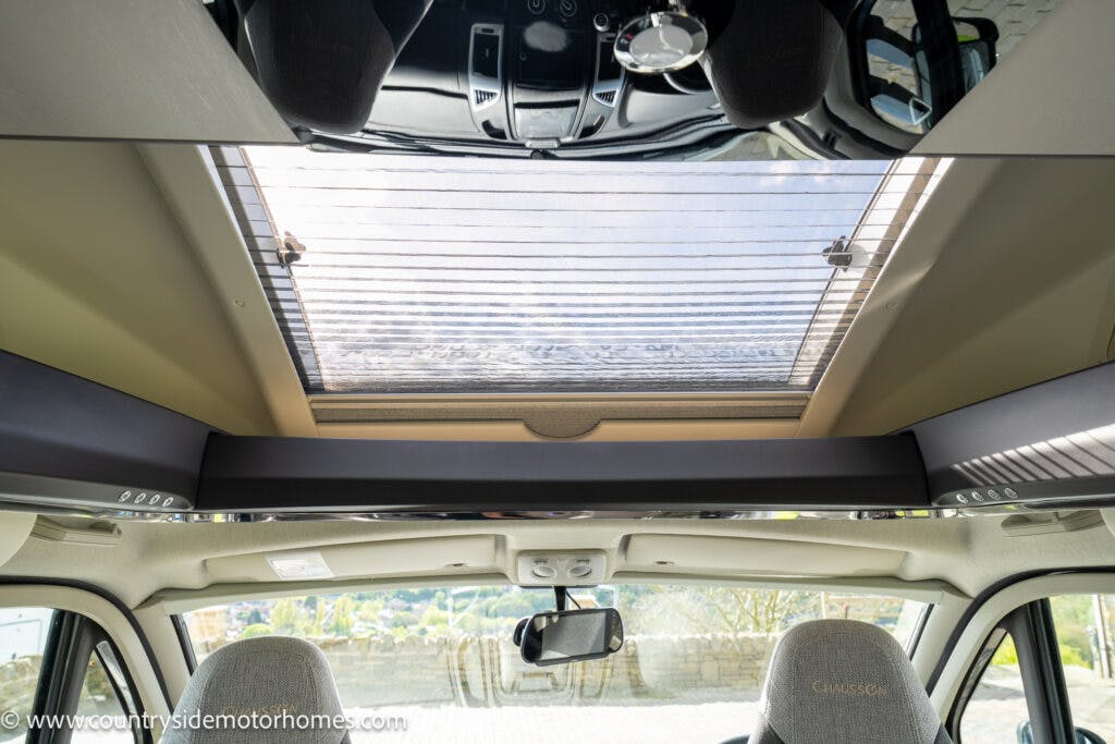 The image shows the interior of a 2021 Chausson 778 Premium motorhome, focusing on a large skylight with a partially open reflective sunshade. The dashboard, rearview mirror, and driver's and passenger's seats are visible at the bottom of the image.
