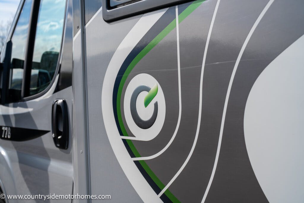 Close-up of the 2021 Chausson 778 Premium motorhome's exterior design featuring sleek gray, green, and white geometric patterns. The design includes a circular emblem with a green arrow. The website "www.countrysidemotorhomes.com" is visible along the bottom edge of the image.