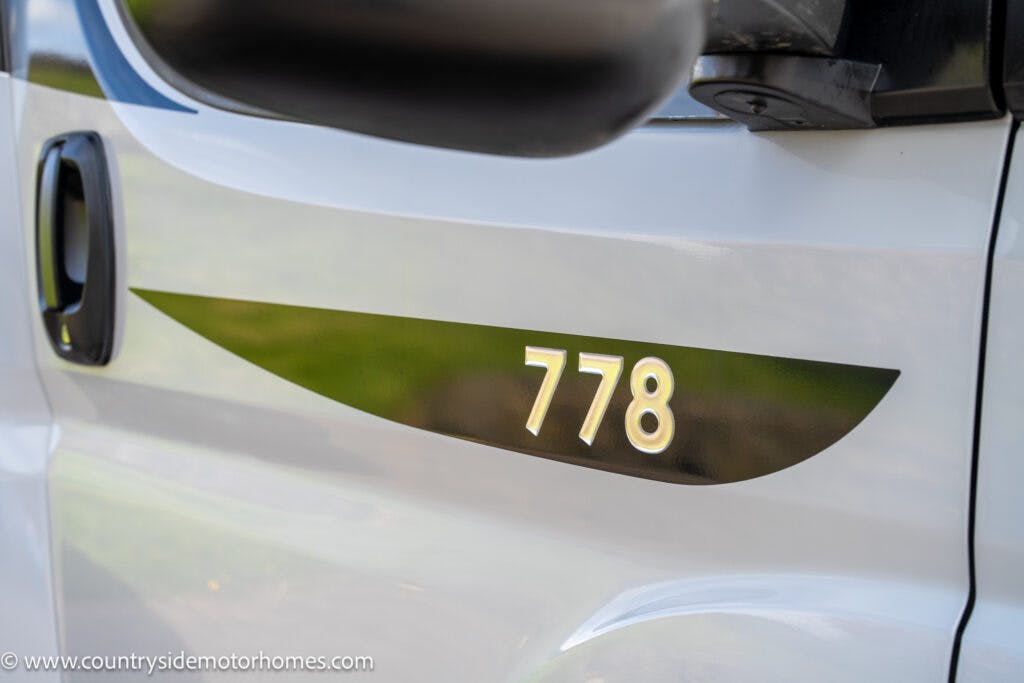 A white 2021 Chausson 778 Premium vehicle with a black and green decal displaying the number "778" on its side. The side mirror and door handle are visible, with the website "www.countrysidemotorhomes.com" partially shown at the bottom left.