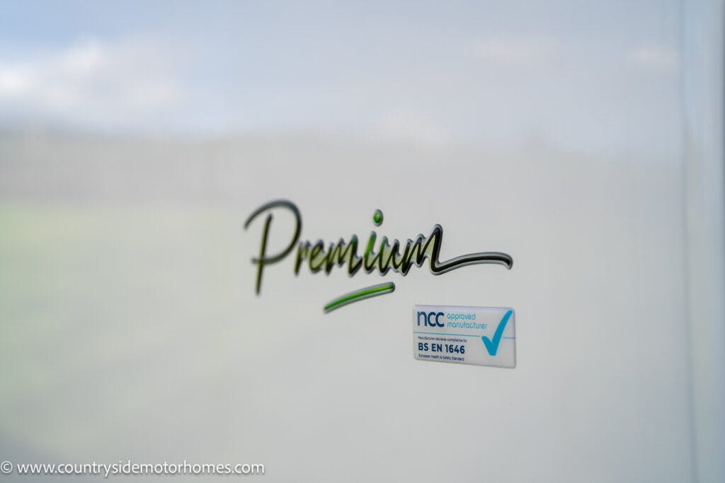 Close-up view of a sign that reads "Premium" and an NCC approved manufacturer label with the code "BS EN 1646" on a smooth white surface. A website URL, www.countrysidemotorhomes.com, is visible at the bottom left corner of the image, showcasing the 2021 Chausson 778 Premium.