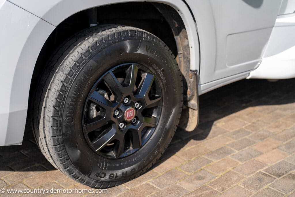 Close-up of a tire on a white 2021 Chausson 778 Premium, highlighted by the Fiat emblem at the center of the black wheel rim. The vehicle is parked on a brick-paved surface. The URL www.countrysidemotorhomes.com is written at the bottom left corner of the image.