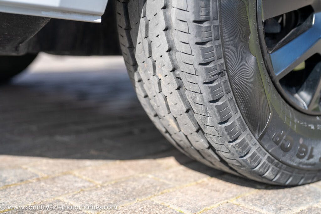 Close-up of a 2021 Chausson 778 Premium tire parked on a cobblestone surface. The tire shows noticeable wear and tread patterns, with some text visible on the sidewall. Part of the vehicle's wheel rim is also visible.