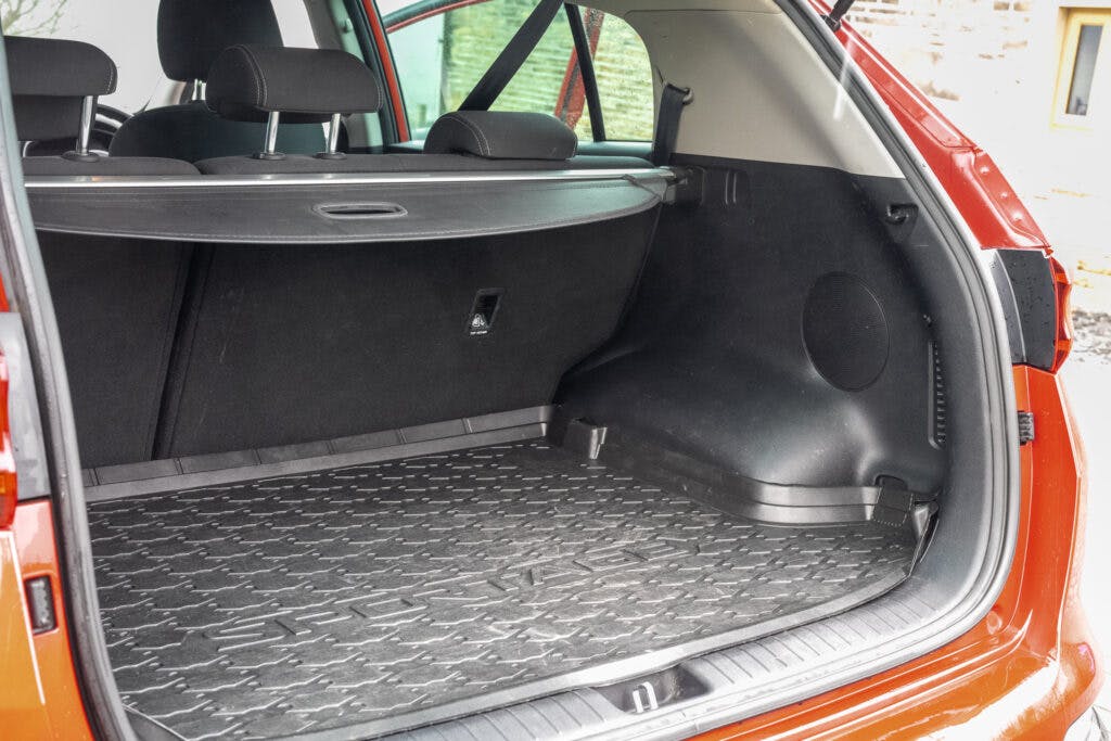 The image shows the rear cargo area of a 2021 Kia Sportage 1.6 GDi 2 with the tailgate open. The cargo area is empty, revealing a black, textured rubber mat and a retractable cargo cover. The interior appears clean and spacious.