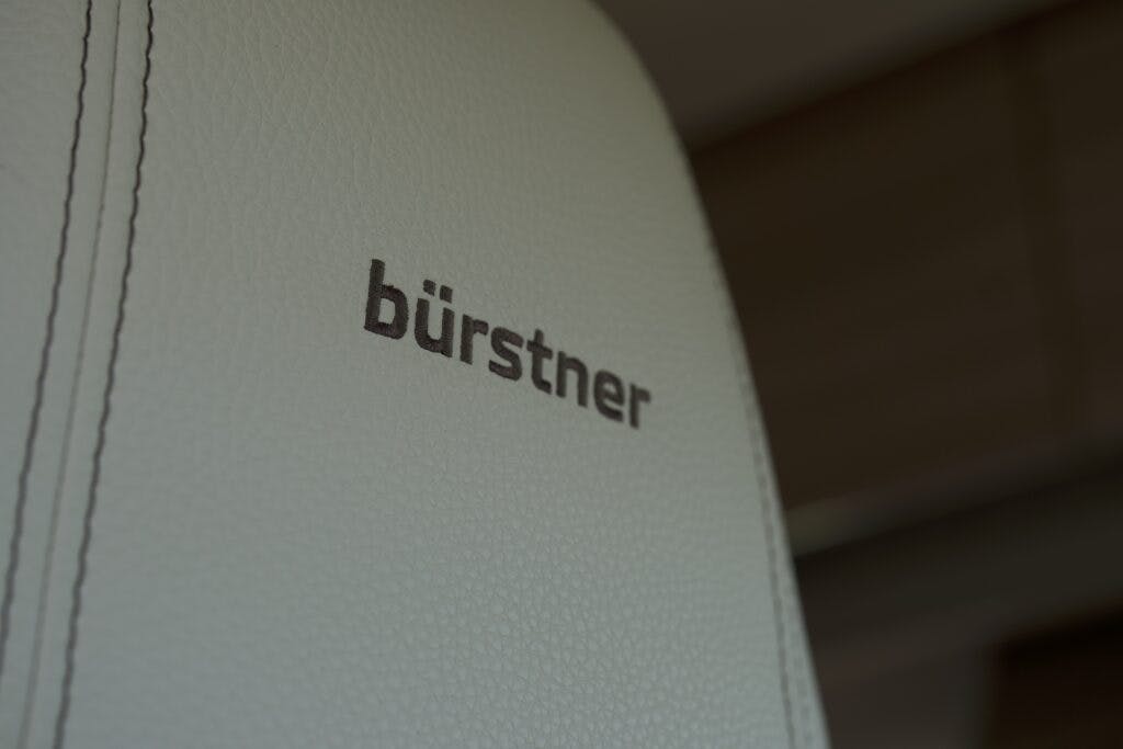 Close-up of a light-colored leather car seat headrest with the word "bürstner" embroidered in dark stitching, in the 2018 Burstner Ixeo TL680 G. The background is blurred.