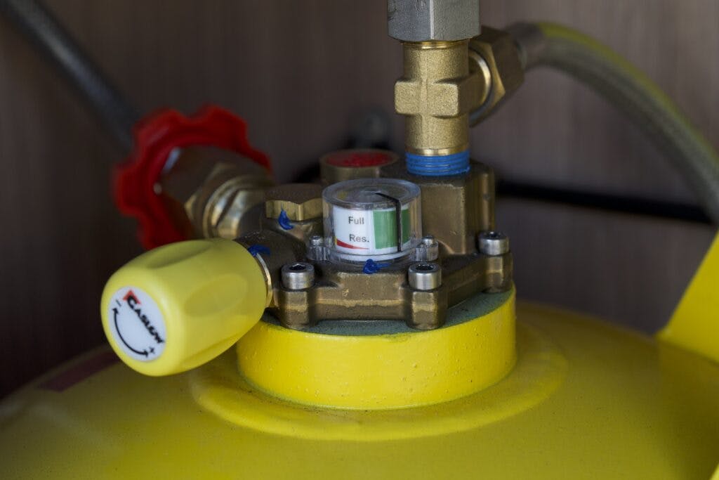 Close-up of a gas pressure gauge attached to a yellow gas cylinder in a 2018 Burstner Ixeo TL680 G. The gauge shows "full" and "res" indicators, with the needle pointing close to "full." Surrounding components include hoses and a red valve.