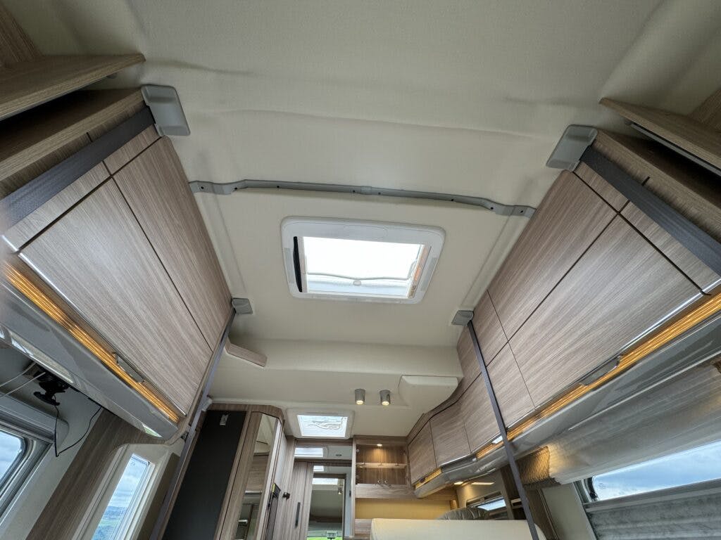 The interior ceiling of the 2018 Burstner Ixeo TL680 G motorhome is visible, featuring wooden storage cabinets on both sides. A skylight is centrally located, with a small light fixture positioned near the center. Walls and ceiling are light-colored, giving the space a clean and modern appearance.