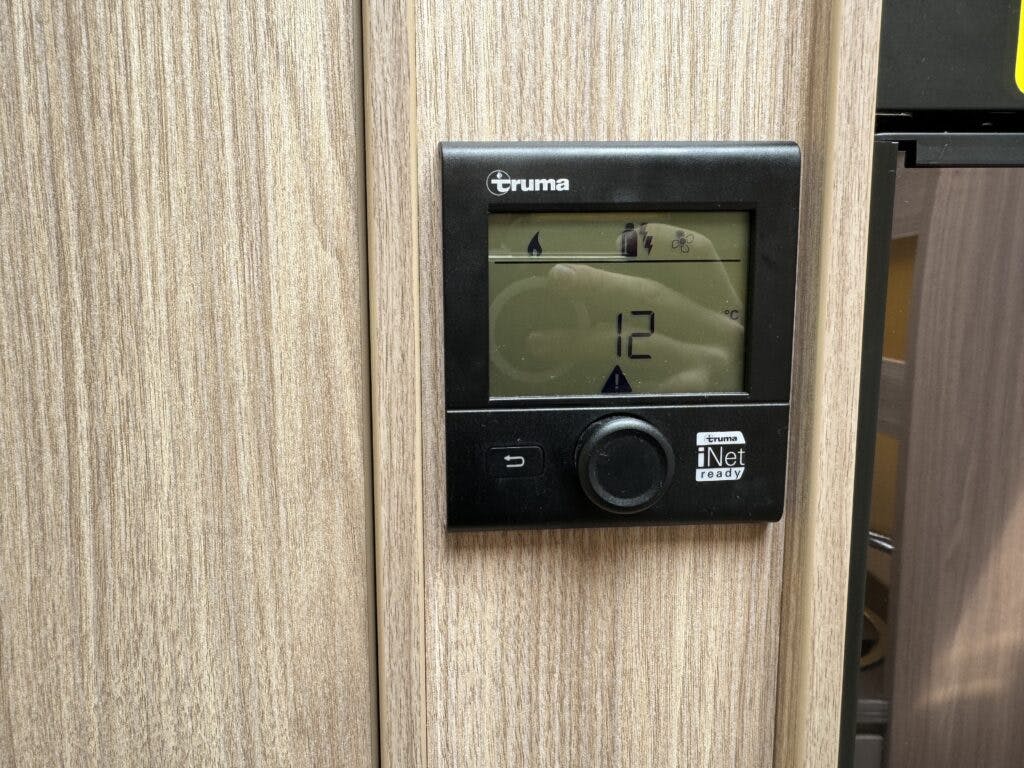 A black Truma iNet ready control panel is mounted on a light wood textured surface inside the 2018 Burstner Ixeo TL680 G. The screen displays the number 12 with various icons above it, indicating settings or statuses.