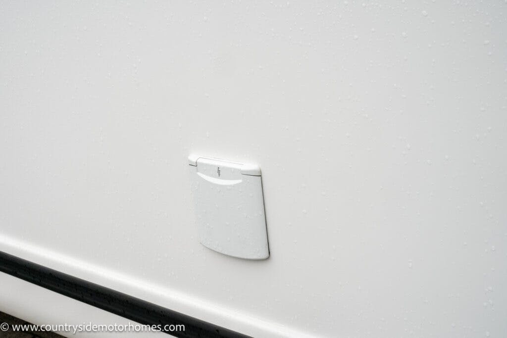 A close-up view of the access panel on a 2022 Benimar Mileo 282, with water droplets visible on the smooth surface. The image features a website URL "www.countrysidemotorhomes.com" in the bottom left corner.