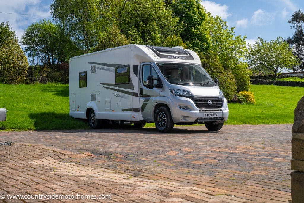 A 2019 Swift Escape 694 Freestyle motorhome is parked on a paved driveway surrounded by a grassy area with trees in the background. The vehicle is primarily white with gray accents, and the website "www.countrysidemotorhomes.com" is visible on the bottom corner. The license plate reads "Y469 DYW.