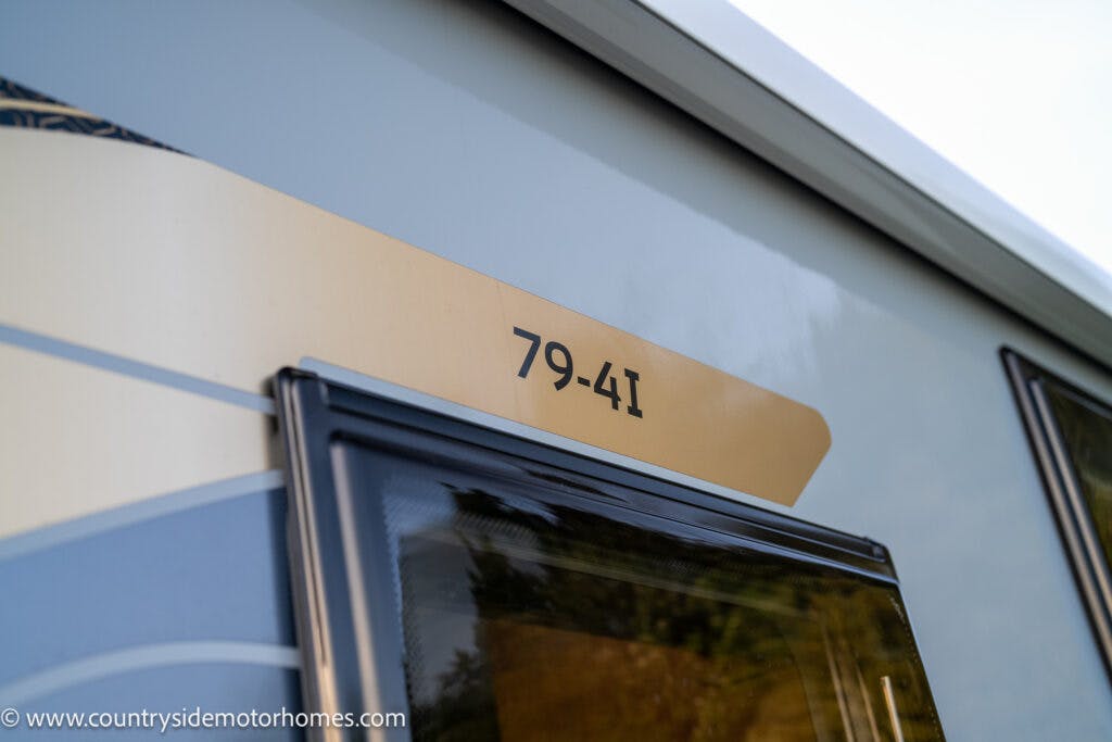 Close-up of an exterior section of a 2021 Bailey Autograph 79-4i motorhome, showing the number "79-41" on a yellow and cream-colored background. The motorhome windows are partially visible, with reflections of the surroundings. The website URL "www.countrysidemotorhomes.com" appears in the bottom left corner.