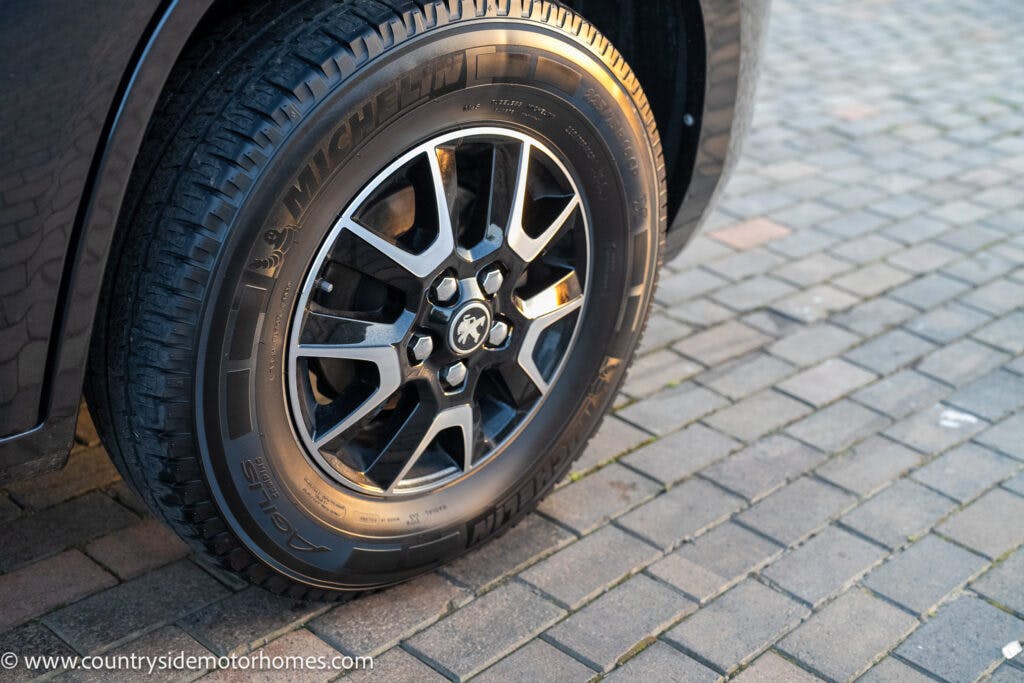 Close-up of a tire and alloy wheel on a 2021 Bailey Autograph 79-4i parked on a cobblestone surface. The tire is branded with “Michelin” and has visible tread patterns. The website "www.countrysidemotorhomes.com" is noted in the bottom left corner of the image.