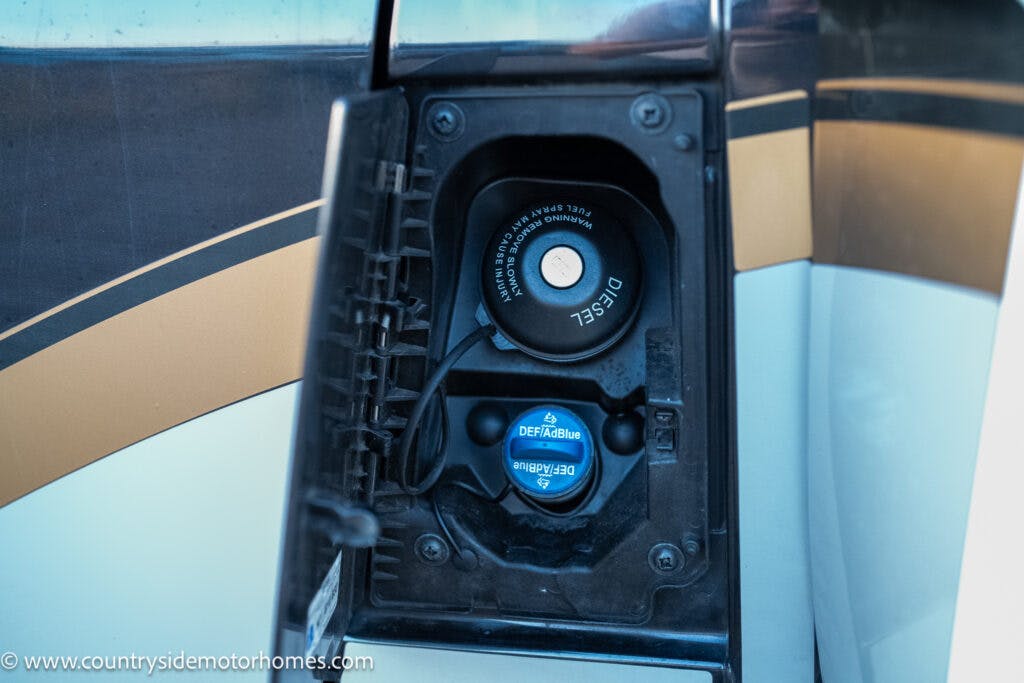 Close-up of the fuel cap area of a 2021 Bailey Autograph 79-4i, featuring two caps; the top one labeled "Diesel" and the bottom one labeled "DEF/AdBlue." The compartment door is open, displaying both caps clearly.