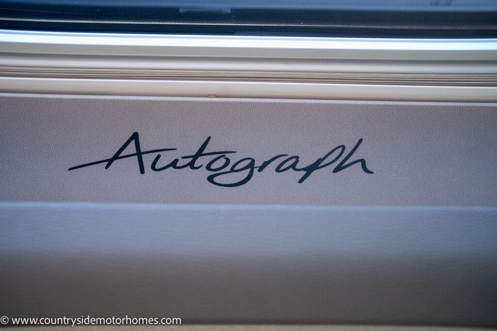The image shows the word "Autograph" written in a stylized cursive font on a beige surface beneath a window, evocative of the 2021 Bailey Autograph 79-4i. The website "www.countrysidemotorhomes.com" is visible at the bottom left of the image.
