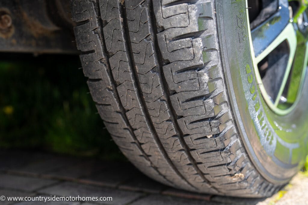 Close-up view of a car tire on a paved driveway, showcasing the tread pattern and worn condition. A portion of the car's wheel and body is visible, hinting at the sturdy build of the 2019 Swift Escape 694 Freestyle. The URL "www.countrysidemotorhomes.com" is in the bottom left corner of the image.