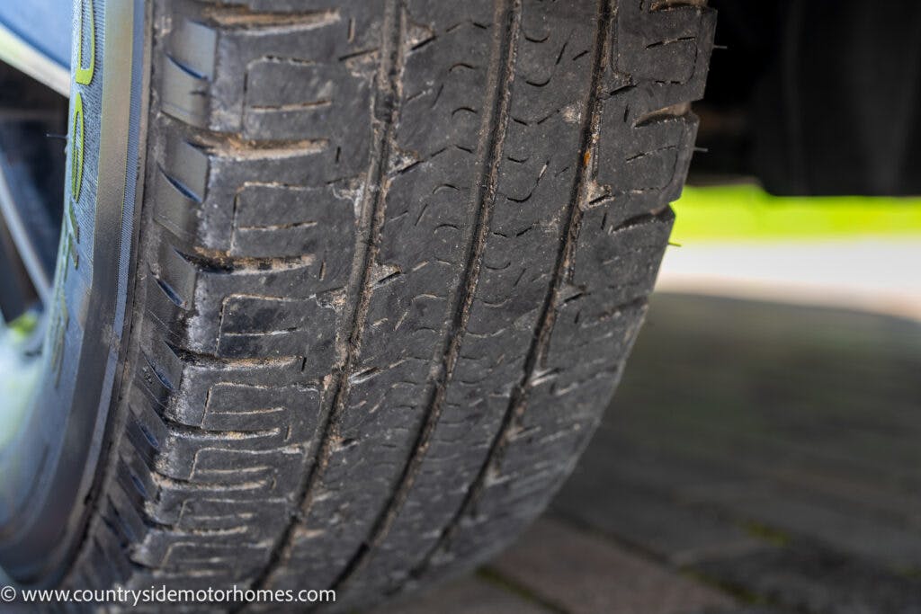 Close-up of a tire with worn tread patterns from a 2019 Swift Escape 694 Freestyle. The tread shows signs of significant wear, including shallow grooves and diminished traction. The image appears to be taken in an outdoor setting on a paved surface.