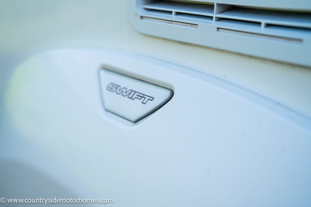 Close-up image of the "SWIFT" emblem on a white vehicle, likely a 2019 Swift Escape 694 Freestyle, with part of an air vent visible above it. The web address "www.countrysidemotorhomes.com" appears in the bottom left corner.