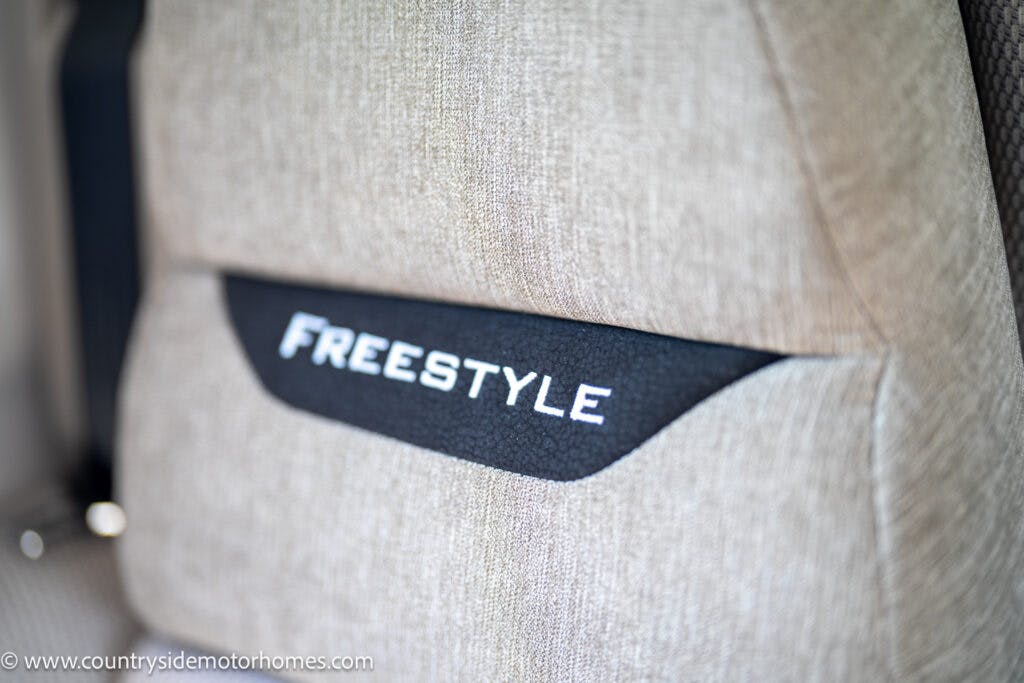 Close-up of a beige car seat in the 2019 Swift Escape 694 Freestyle, featuring the word "FREESTYLE" on a black strip in the center. The image also includes a portion of a seatbelt on the left side and a web address "www.countrysidemotorhomes.com" at the bottom.