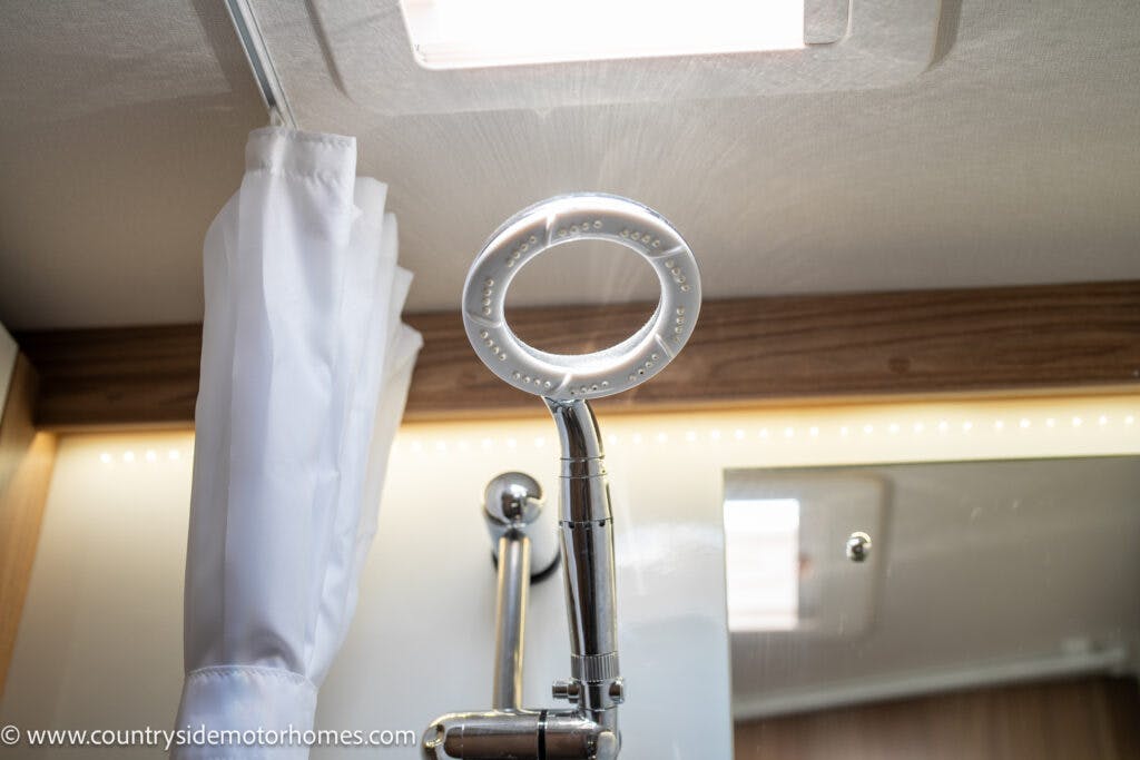 A modern showerhead is mounted in a bathroom with light wood paneling. A white shower curtain hangs to the left, and a rectangular light fixture adorns the ceiling. The logo for Countryside Motorhomes is visible in the bottom left corner, indicating this is part of the 2019 Swift Escape 694 Freestyle model.
