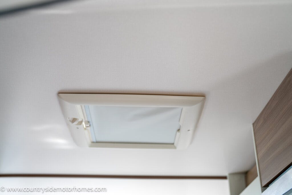 A ceiling-mounted hatch with a closed frosted window in a room with light-colored walls, reminiscent of the stylish accents found in the 2019 Swift Escape 694 Freestyle. A small latch is visible on the left side of the window.
