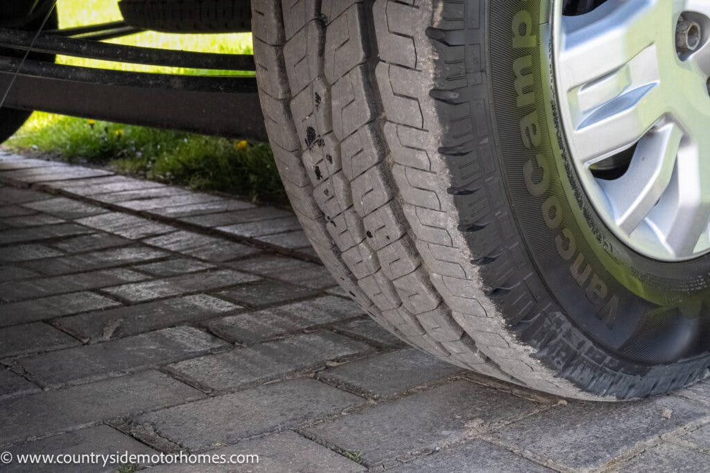 Close-up image of a 2021 Auto-Sleepers Broadway EL tire resting on a brick-paved surface. The tread and sidewall of the tire are clearly visible, as is part of the wheel rim. The website "www.countrysidemotorhomes.com" is visible in the bottom-left corner.