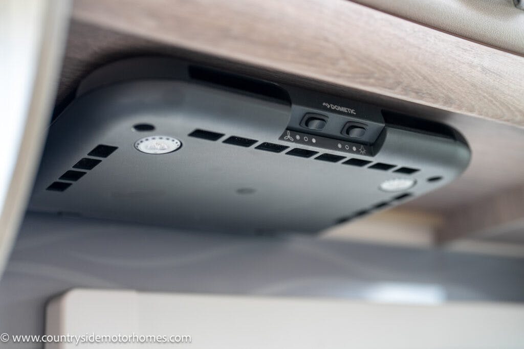 A black Dometic ventilation unit, installed underneath a wooden shelf in the 2021 Auto-Sleepers Broadway EL motorhome, features several buttons and vents. The website www.countrysidemotorhomes.com is visible in the bottom left corner.