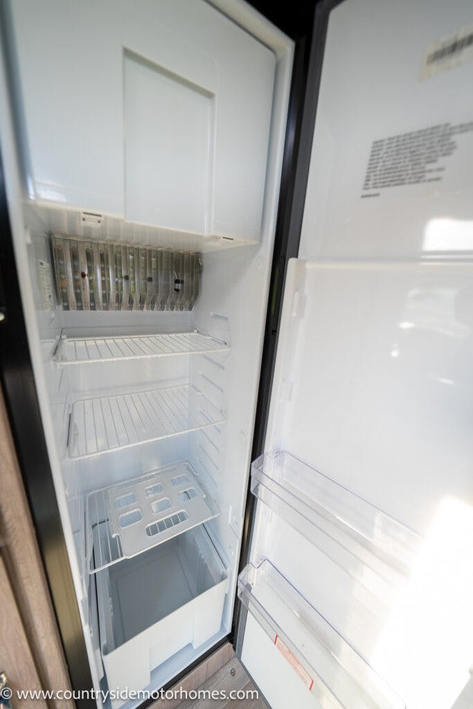 An open refrigerator with empty shelves and compartments. The door also has empty shelves. The fridge, reminiscent of the tidy storage in a 2021 Auto-Sleepers Broadway EL, is clean and well-lit, revealing the interior clearly.